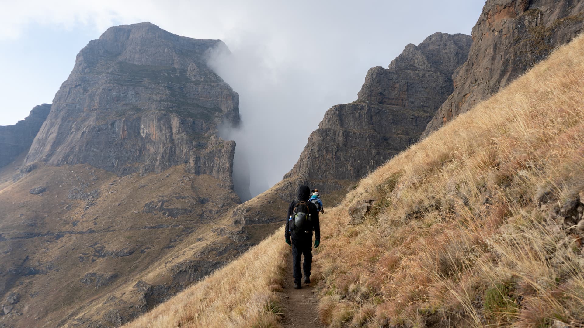 Hikers walking a mountain trail toward a misty gorge